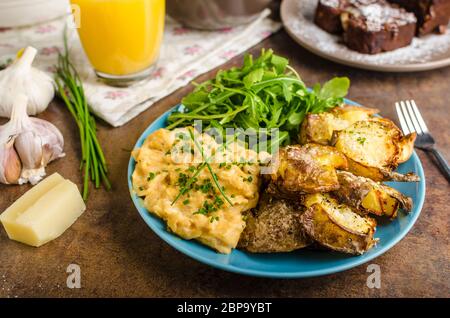 Knusprige zerschlagen Kartoffeln, Rührei und kleinen Salat, Saft und Kuchen zum Frühstück Stockfoto