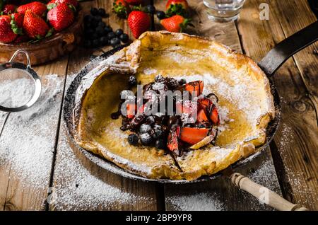 Holländische Baby-Pfannkuchen mit Beeren und Schokolade, gebacken im Ofen auf Eisenpfanne, besten Pfannkuchen immer!!! Stockfoto