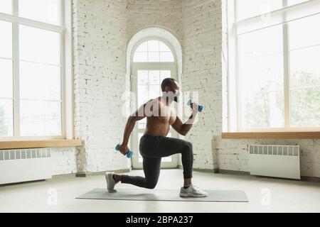 Junger afroamerikanischer Mann trainiert zu Hause während der Quarantäne des Coronavirus Ausbruch, doinc Übungen der Fitness, Aerobic. Sportivfähigkeit während der Isolierung. Wellness, Bewegungskonzept. Sit ups. Stockfoto