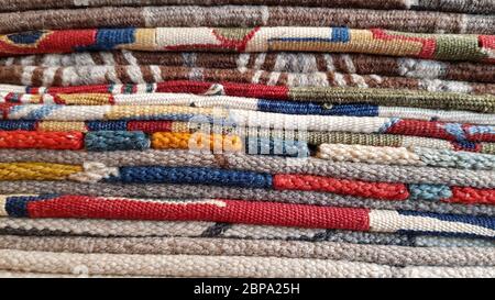 Stapel gefalteter traditioneller türkischer Teppiche. Schichten von bunten gewebten Teppichen. Gewebte Garn texturierte Hintergrund. Kanten von ethnischen Vintage-Teppichen. Haufen ha Stockfoto