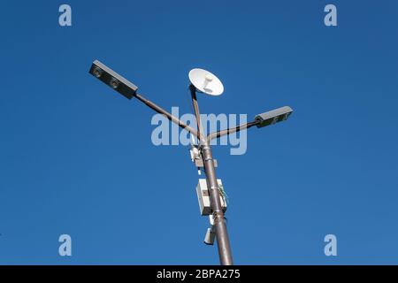 Lampost mit einer darauf montierten Antenne. Säule gegen den blauen Himmel. Stockfoto