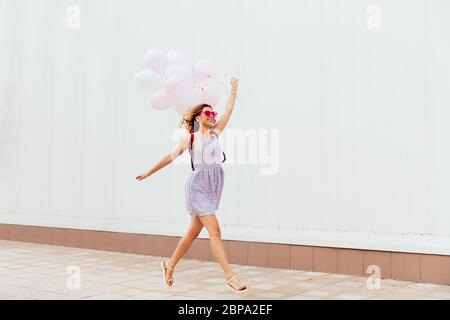 Aufgeregt lächelnde Mädchen in rosa Sonnenbrille mit Luftballons, das Tragen von Kleidung und Sandalen. Im Freien. Stockfoto