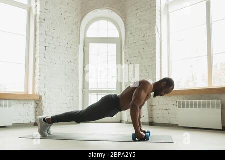 Junger afroamerikanischer Mann trainiert zu Hause während der Quarantäne des Coronavirus Ausbruch, doinc Übungen der Fitness, Aerobic. Sportivfähigkeit während der Isolierung. Wellness, Bewegungskonzept. Plank. Stockfoto