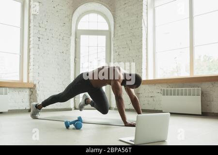 Junger afroamerikanischer Mann trainiert zu Hause während der Quarantäne des Coronavirus Ausbruch, doinc Übungen der Fitness, Aerobic. Sportivfähigkeit während der Isolierung. Wellness, Bewegungskonzept. Plank. Stockfoto