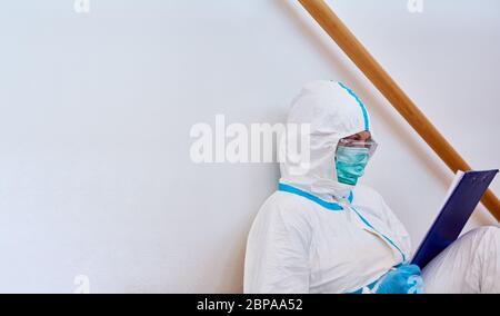 Pflegepersonal in der Klinik in Schutzkleidung Studien Liste auf dem Klemmbrett während der Pause auf dem Boden während Coronavirus-Epidemie Stockfoto