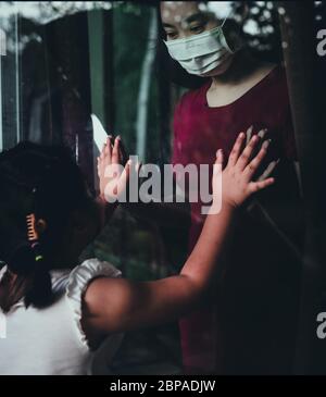 Mutter tragen Gesichtsmaske Treffen Tochter und berühren die Hand durch das Fenster wegen der Quarantäne Corona Virus Covid-19, soziale Distanzierung Stockfoto