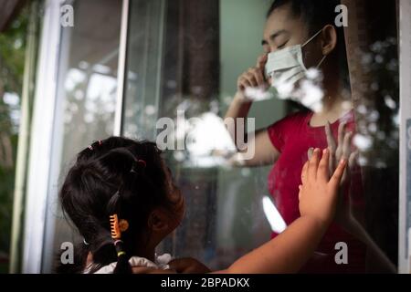 Mutter tragen Gesichtsmaske Treffen Tochter und berühren die Hand durch das Fenster wegen der Quarantäne Corona Virus Covid-19, soziale Distanzierung Stockfoto