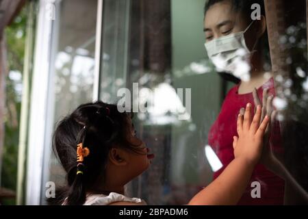 Mutter tragen Gesichtsmaske Treffen Tochter und berühren die Hand durch das Fenster wegen der Quarantäne Corona Virus Covid-19, soziale Distanzierung Stockfoto