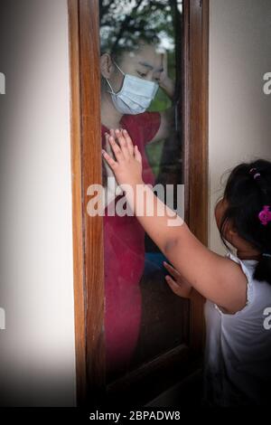 Mutter tragen Gesichtsmaske Treffen Tochter und berühren die Hand durch das Fenster wegen der Quarantäne Corona Virus Covid-19, soziale Distanzierung Stockfoto