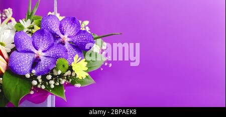 Schöner Blumenstrauß in lila Holzkorb auf lila Hintergrund. Orchideen, Chrysanthemen, Lilien, Kamillen floristische Zusammensetzung Stockfoto