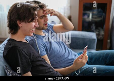 Zwei Brüder plaudern in Corona-Tagen per Smartphone mit ihrem Vater, sind glücklich und lachen. Stockfoto
