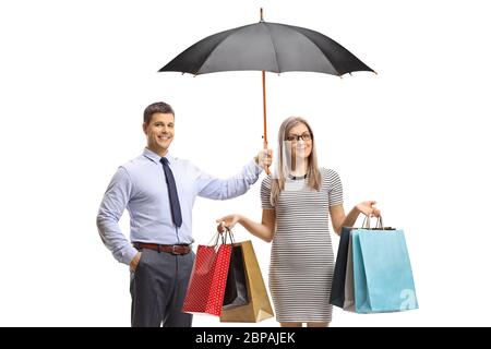 Mann, der einen Regenschirm über einer jungen Frau hält, mit Einkaufstaschen auf weißem Hintergrund isoliert Stockfoto