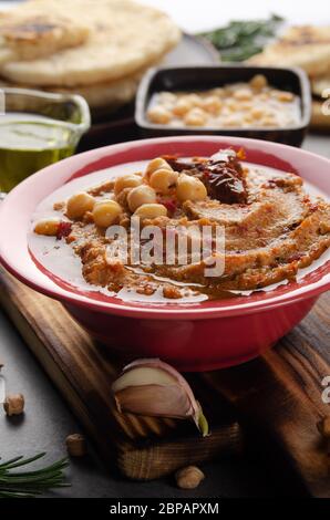 Frischer hausgemachter Hummus in Tonform mit Olivenöl, Kichererbsen, Gewürzen und sonnengetrockneten Tomaten auf Steintisch Stockfoto