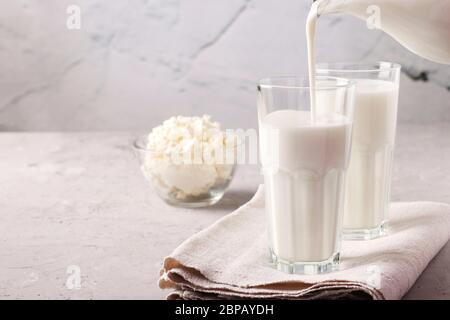 Kefir oder Ayran fermentierten Getränk wird in ein Glas aus einem Krug, sowie Quark in einer Schüssel auf einem hellgrauen Hintergrund gegossen, Close Up, Space Stockfoto