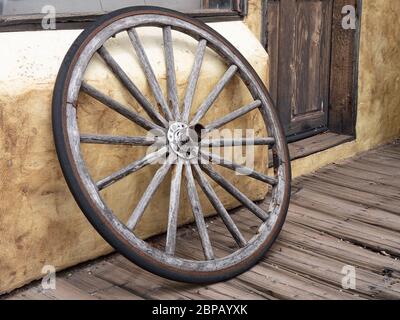 Altes hölzerner Wagenrad, das sich an einer Außenwand auflehnte. Stockfoto