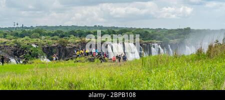 Victoria Falls, Zimbabwe - 4. Februar 2020 : Victoria Falls am Zambezi Fluss, Grenze von Sambia und Simbabwe mit Touristen am Wasserfall Stockfoto