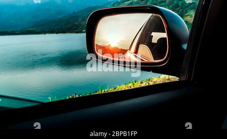 Selektiver Fokus Rückspiegel eines Autos, der den Sonnenuntergang reflektiert. Sonnenuntergang im Rückspiegel. Schöner See und Sonnenuntergang Reflexion durch Car Side mir Stockfoto