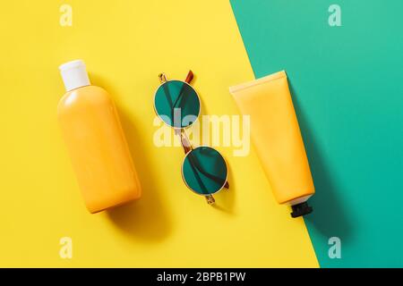 Sommer helle Flatlay auf bunten Hintergrund mit Röhren und Flasche mit Sonnencreme, grüne Sonnenbrille. Harte Schatten und Licht. Draufsicht. Flaches Lay. Trend Stockfoto