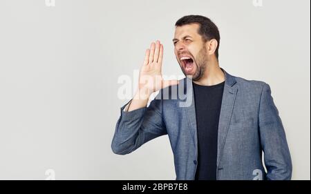 Ein junger Mann mit Bart schreit laut mit der Hand nahe seinem Mund. Das Konzept der Kommunikation, Nachrichten und Aufmerksamkeit zu erregen. Stockfoto