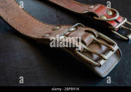 Fragment von zwei alten echten Lederhalsbändern auf einem dunklen Tisch. Zerbrochene, schäbige Leder- und Metallbeschläge. Echte Vintage Hundehalsbänder. Liebe zu den Tieren. Stockfoto