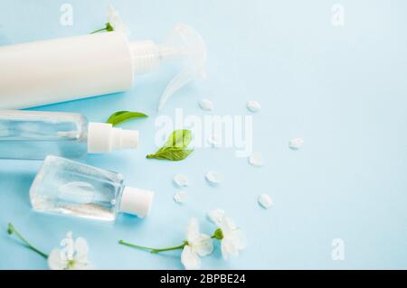 Hand antiseptisch in verschiedenen Flaschen und wunderschön blühende Kirschbaum Blumen auf blauem Hintergrund mit Copyspace. Stoppen Sie das Coronavirus-Konzept. Stockfoto