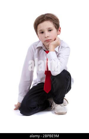 Das Kind sitzt auf einem weißen Hintergrund. Dressy Junge in einem weißen Hemd isoliert. Sieben Jahre altes Kind in Krawatte. Grundschüler. Stockfoto