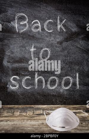 Tafel mit 'zurück zur Schule' Botschaft und schützende Gesichtsmaske auf Holztisch COVID-19 Konzept Stockfoto