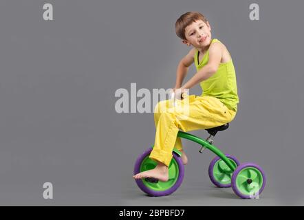 Das Kind auf einem Dreirad auf grauem Hintergrund. Der kleine Junge spielt.der Junge fährt mit dem Fahrrad. Stockfoto