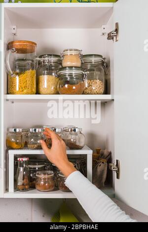 Woman Hand öffnet Küchenregal mit verschiedenen Getreide und Samen in Glasgefäßen auf den Regalen in der Küche Stockfoto