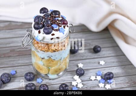 Gesunde Snacks aus Joghurt und Bananen und Heidelbeeren Früchte mit sternförmigen Zucker und Schokolade Streusel in Glas auf Holzhintergrund gekrönt Stockfoto