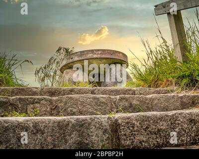 Denkmal aus einem alten Mühlstein, drei große Steine mit einem großen runden Mühlstein auf der Oberseite. Sonnenuntergang im Hintergrund. Stockfoto