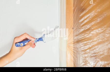 Menschliche Hand malt mit einem Pinsel auf den Rand eines Türrahmens Handwerk Renovierung Übergabe Wohnung Schaden frisch lackiert weiße Wand-Werkzeuge tun es sich Stockfoto