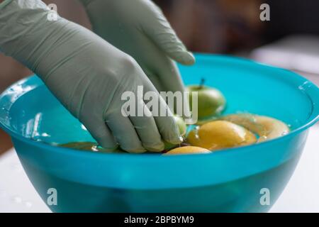 Waschen von Früchten in einer Schüssel mit Plastikhandschuhen. Früchte werden nach dem Einkaufen in einer grünen Schüssel auf Wasser gelegt. Stockfoto