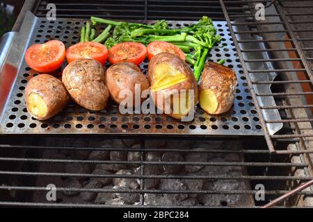 Gemüse auf einem Holzkohlegrill. Ganze rote Kartoffeln Tomaten Brokkoli grüne Bohnen über lumpwood Kohle gegrillt Vegetarisch glutenfreie Zubereitung von Speisen Stockfoto