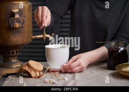 Seitenansicht der weiblichen Hände Gießen Tasse Tee aus Vintage Samowar und Glas hausgemachte Marmelade, Tee Party-Konzept Stockfoto