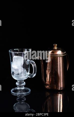Kupferkaffeekanne und leeres Latte Glas mit Eis, kaltes Kaffeekonzept auf schwarzem Hintergrund Stockfoto