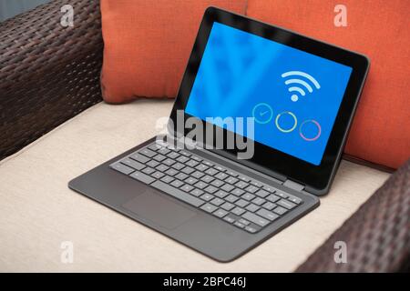 Ein Laptop mit sicherer WiFi-Verbindung zum Heimnetzwerk auf einem Korbsessel, um außerhalb des Büros zu arbeiten. Stockfoto