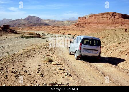 Eine unbefestigte Straße führt durch die trockene, atemberaubende Landschaft in der Nähe von Skoura im Süden Marokko. Im Hintergrund der Hohen Atlas. Stockfoto