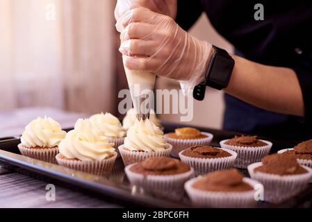 Schokolade Cupcakes mit einem Strudel Sahne.Weibliche Hände füllen Cupcakes auf einem Backblech. Stockfoto