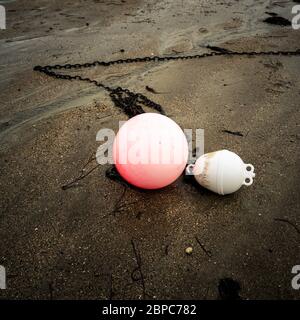 Nahaufnahme einer rosa und einer weißen Boje und ihrer Ankerketten, die auf dem nassen Sand am Strand, Bretagne, Frankreich liegen Stockfoto