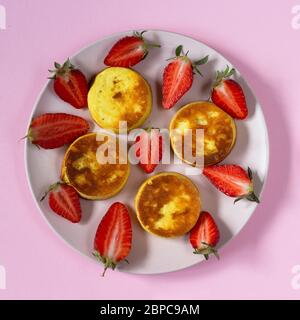 Hausgemachte Cottage Cheese Pancakes mit Erdbeere auf rosa Hintergrund. Draufsicht. Stockfoto