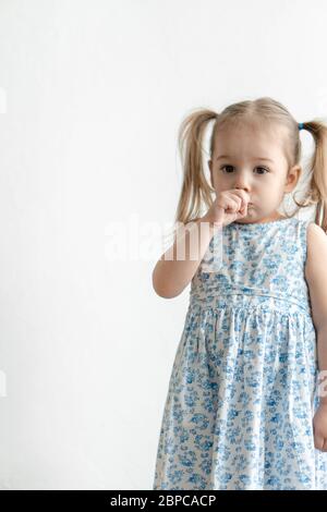 Kindheit, Emotionen Konzept - mittel Plan Isolieren kleine süße drei-jährige Mädchen mit zwei Pferdeschwänzen in einem blauen Kleid bläst in eine Faust und zeigt Stockfoto