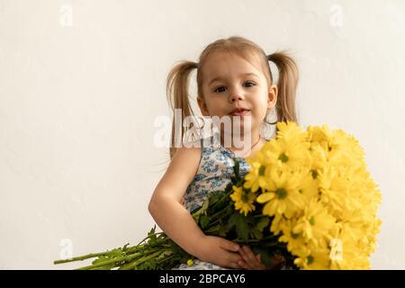 Kindheit, Feiertage, Blumen, Geschenke Konzept - kleine süße drei-jährige Mädchen mit zwei Pferdeschwänzen auf dem Kopf in blau bunten Kleid hält groß Stockfoto