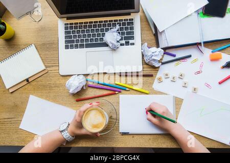 Draufsicht weibliche Hände halten Stift und Kaffee über weiß leere Notizbuch für neue kreative Ideen. Arbeitsplatz mit Laptop, Rohlinge, bunte Papeterie und Stockfoto