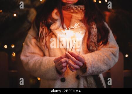 Eine junge Frau mit Funkeln, die am weihnachtsbaum in der Stadt steht Stockfoto