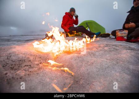 Lagerfeuer bewegt sich über den Gletscher, als zwei Männer auf einem Gletscher zelten. Stockfoto