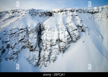 Luftaufnahme der Bergkette mit rauen steilen Hängen mit Schnee in Island bedeckt Stockfoto