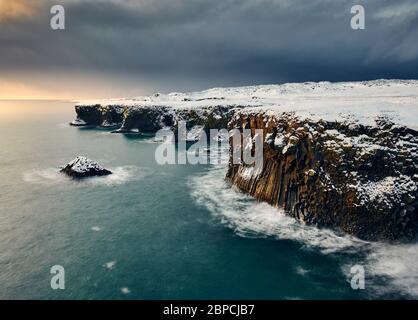 Drohne Blick auf die malerische Landschaft der felsigen Klippe mit Schnee auf dem Hintergrund des stürmischen Himmels in Island bedeckt Stockfoto