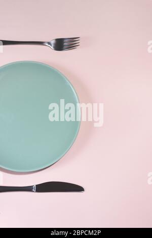 Oben in der Nähe auf der Ansicht der Gabel, leere Porzellan grüne Platte und Messer auf dem rosa Hintergrund gesetzt. Stockfoto