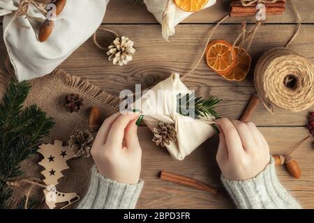 Zero Waste und umweltfreundliches weihnachtskonzept. Weibliche Hände wickeln Geschenke in Naturstoff mit Ornamenten aus natürlichen Materialien, Draufsicht, flach legen Stockfoto